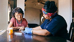 Developing an Indigenous systems alignment framework: A call for direct funding. Stock image shows elderly indigenous woman talking to an indigenous health worker